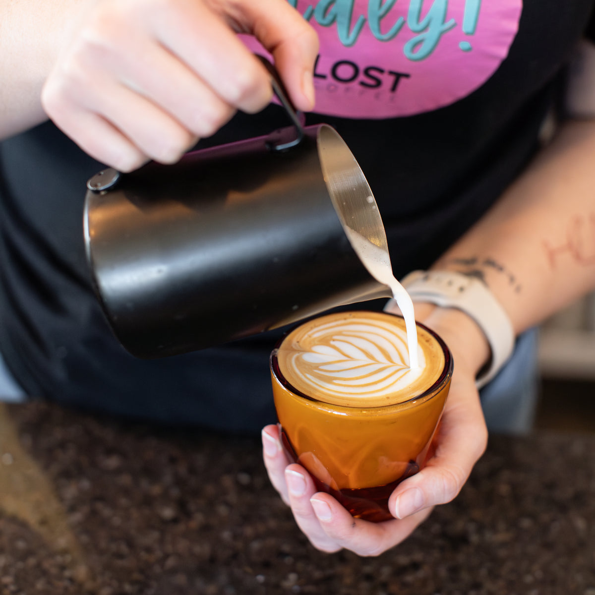 A female barista doing latte art on a cortado with six stacks and a heart
