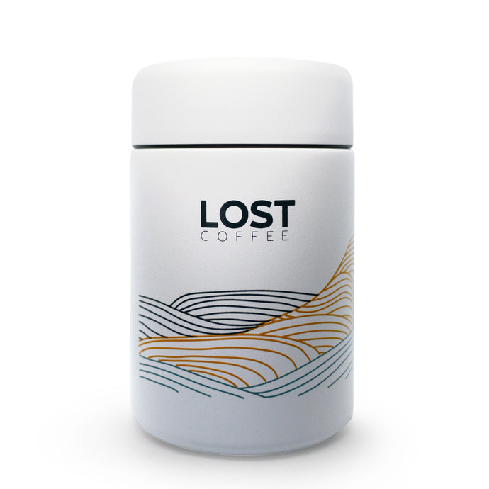A white coffee canister by Lost Coffee with thin line art that is orange, blue, and black